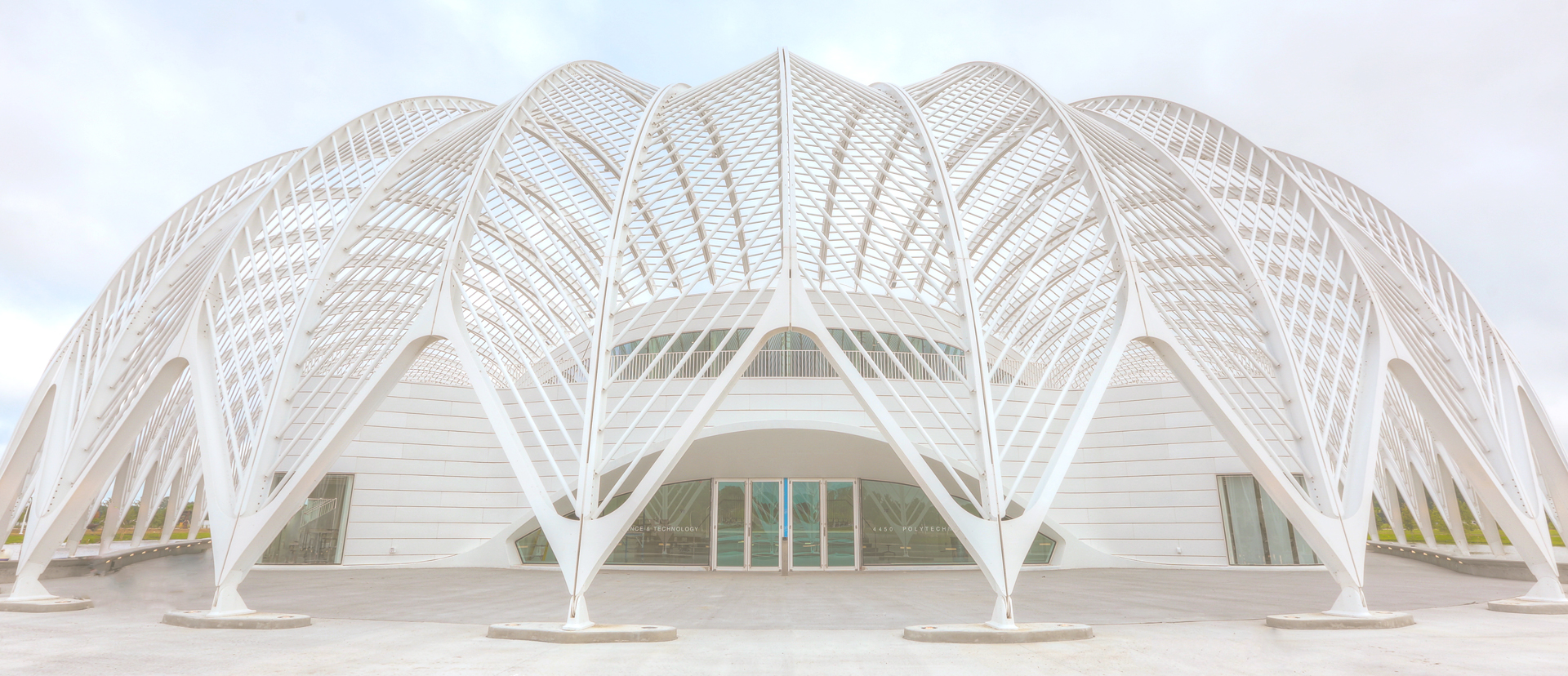 A white building wrapped in sweeping arched steel ribs, seen from the front